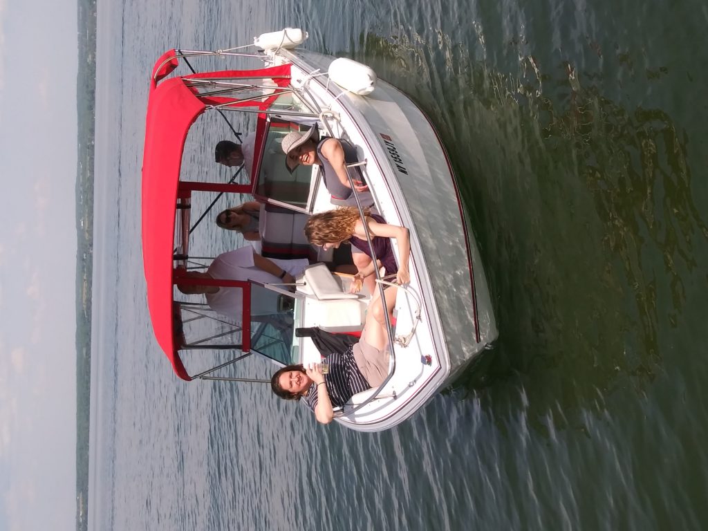 A group of people sits in the bow of a white 23-foot Chris Craft boat, sipping wine on a bright sunny day. - Bianconi Tours