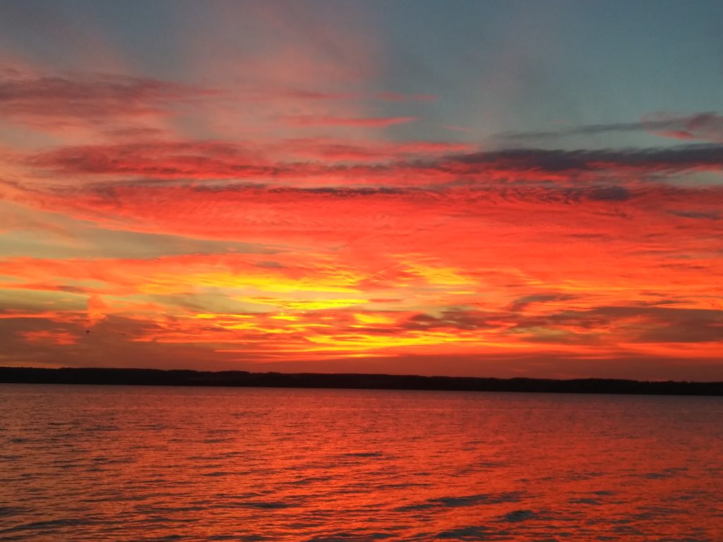 Bright orange, red, and yellow colors reflect on the clouds and on Cayuga Lake's waters as the sunsets.